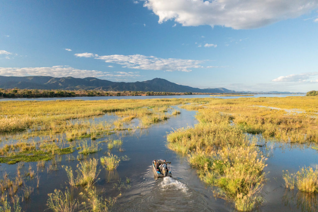 An aerial view of a boat cruising through wetland channels with mountains rising in the distance.