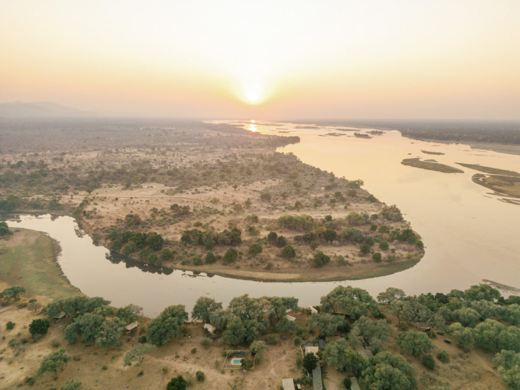 Aerial view of the Zambezi River at sunrise, winding past the camp nestled among riverside trees.