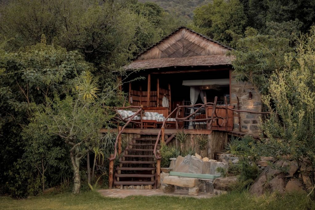 Exterior of a guest room at Desert Rose, with branch-railed wooden steps rising to a deck of striped loungers beside a stone wall.