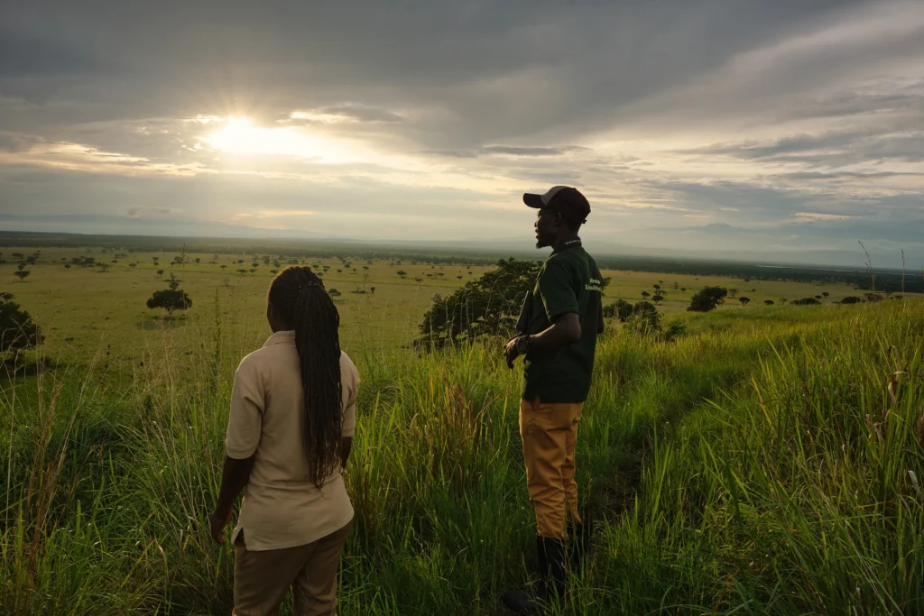 Two guides looking out over the savannah of Queen Elizabeth National Park at sunset from the Fig Tree Trail near Kyambura Gorge