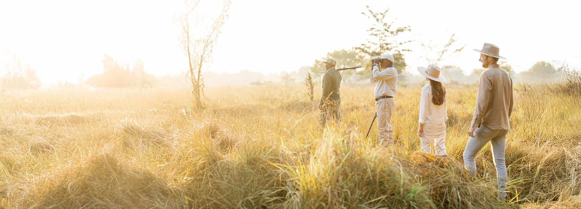 Guests and guides pause during a walking safari at Time + Tide Luwi Camp in South Luangwa National Park, watching the bush come alive in the soft morning light.