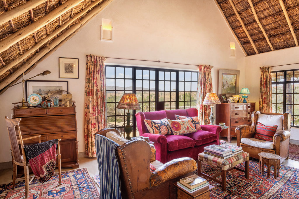 West Wing sitting room with a magenta velvet sofa, leather club chairs, a roll-top desk and steel-framed windows looking out over hills.