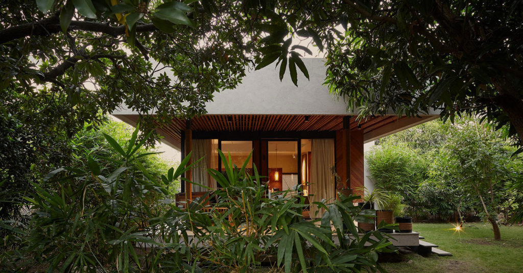 A garden villa with thatched-style roof set among trees at Woods at Sasan Gir
