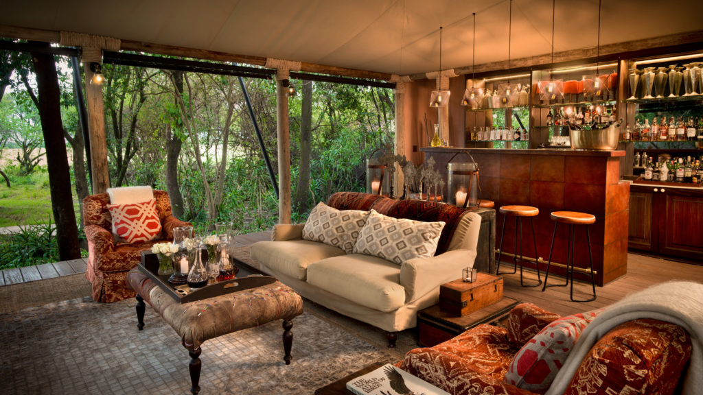 A lounge and bar area furnished with patterned armchairs, leather stools and safari curios