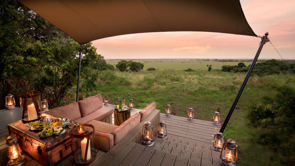 Lanterns line a private deck set for sundowners, overlooking the open grasslands of the Mara