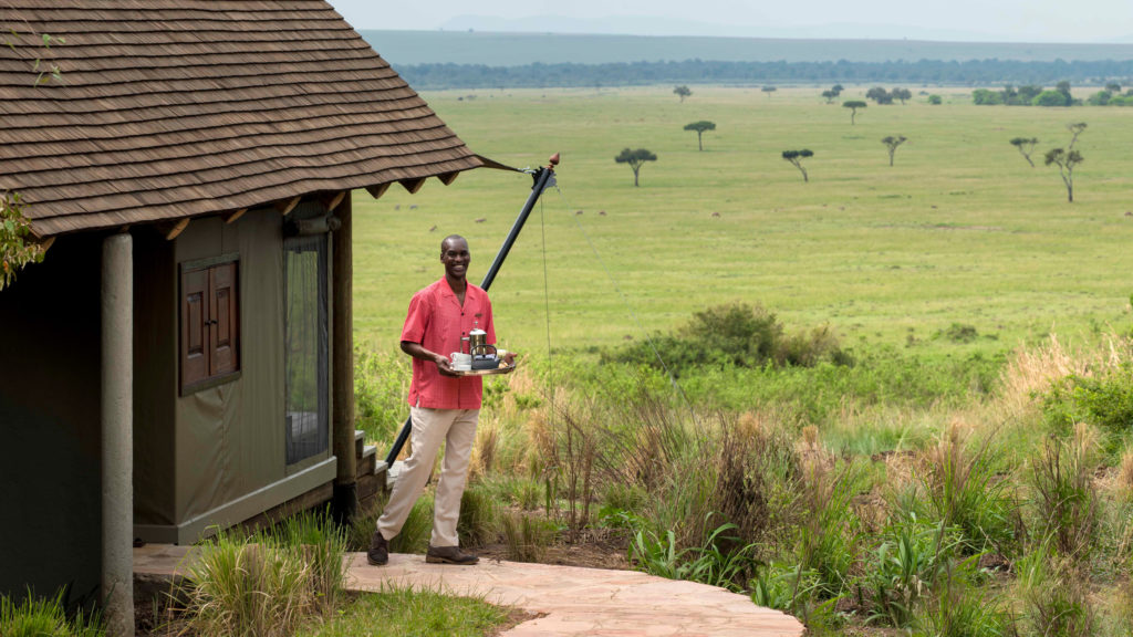 A camp butler carries coffee and tea to a guest tent overlooking the plains at Bateleur Camp