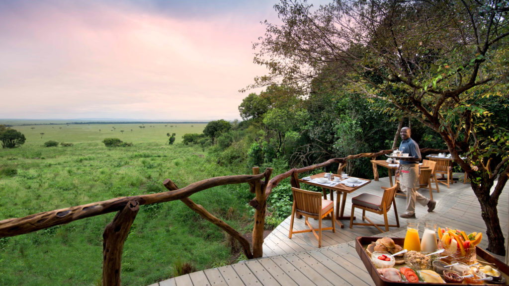 A waiter carries breakfast to a table set on a deck overlooking the grasslands at sunrise