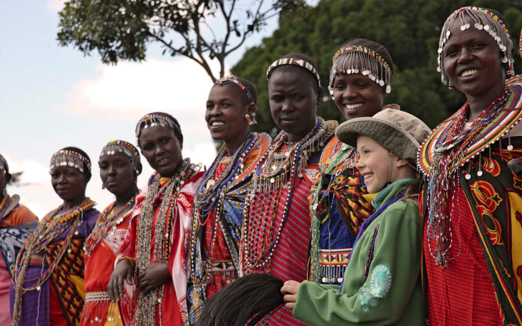 A young guest joins a group of Maasai women in traditional beaded dress during a village visit