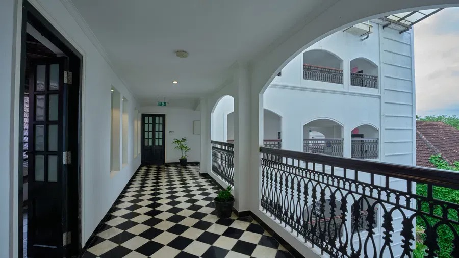 An arched colonial corridor with black-and-white checkered flooring and wrought-iron balcony railings overlooking the courtyard.