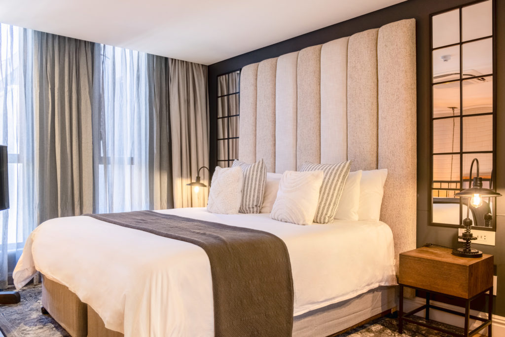 Upholstered headboard and bed at The Weinberg with bedside lighting and window mirror reflecting the valley view