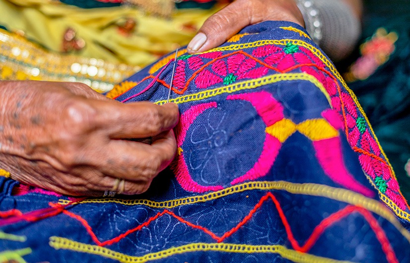 Close-up of hands hand-stitching colourful mirror-work embroidery