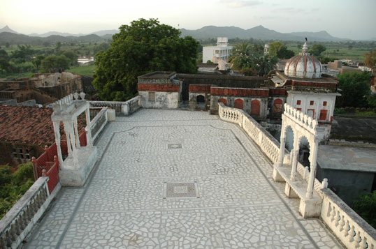 Views across the Aravalli hills and Poshina village from the fort's stone rooftop terrace, framed by domed pavilions at dusk