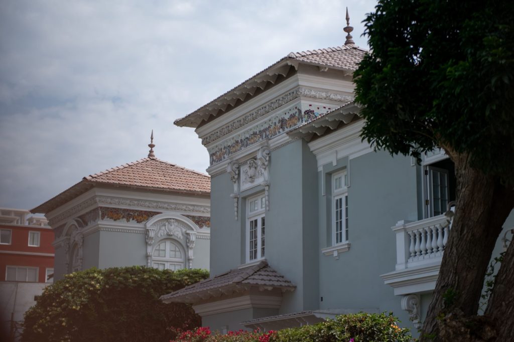 Mint-green colonial villa with ornate mosaic cornicing, tiled hip roofs and finial spires against a cloudy sky