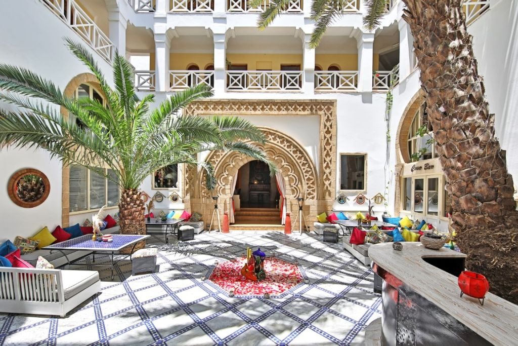 The courtyard of this Essaouira riad, a towering date palm framed by carved archways and tiered white balconies.