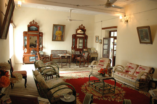 A heritage sitting room at Darbargadh Poshina, furnished with antique mirrored cabinets, framed portraits and period cane chairs