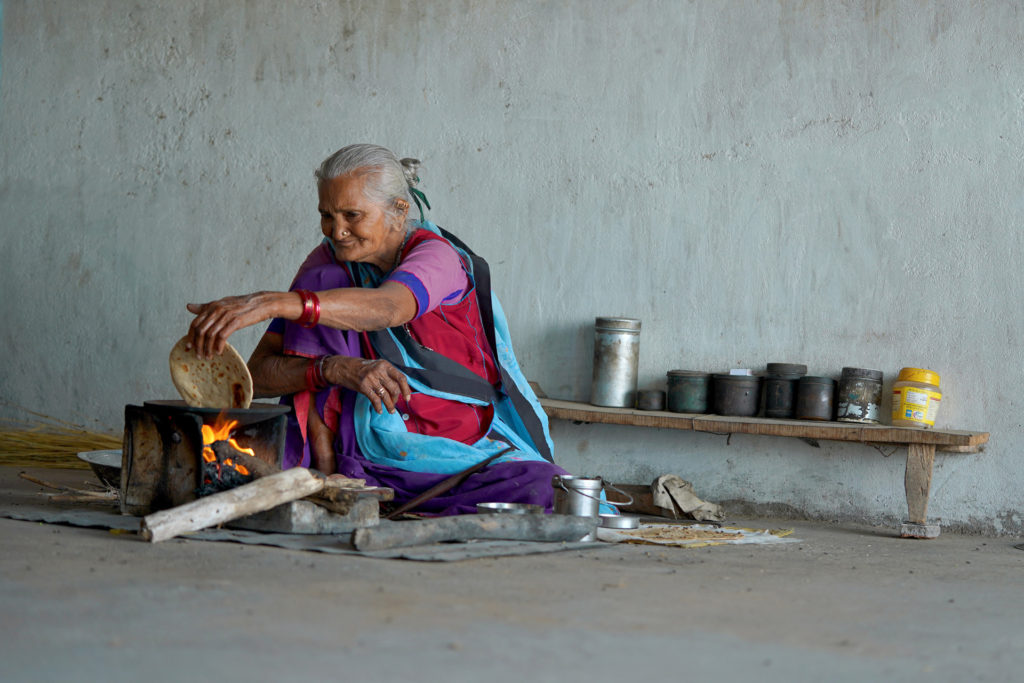 An elderly woman making chapati over an open fire