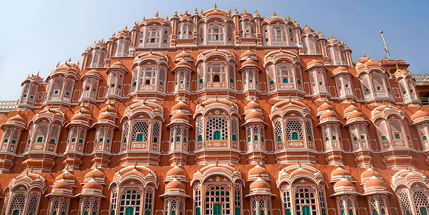 The ornate façade of the Hawa Mahal in Jaipur, showcasing its iconic honeycomb of pink sandstone windows built for royal women to observe city life unseen. 