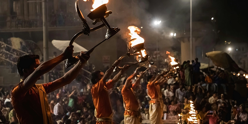 Hindu priests performing the Ganga Aarti ceremony in Varanasi, lifting flaming lamps in unison along the sacred ghats of the River Ganges. 