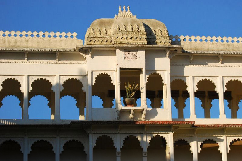 Scalloped stone arches and a domed pavilion crown the sunlit facade of Darbargadh Poshina against a clear sky