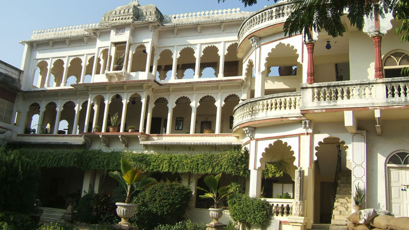 The arched, multi-storey facade of Darbargadh Poshina framed by lush garden greenery under a bright blue sky