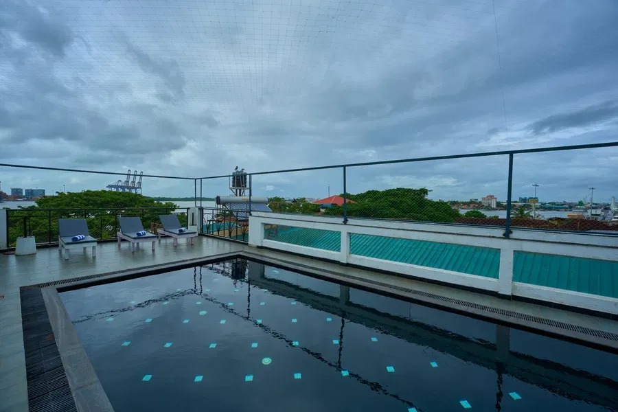 A wider view of the sea-view rooftop pool at The Old Court House, overlooking Fort Kochi's coastline under a cloudy sky.