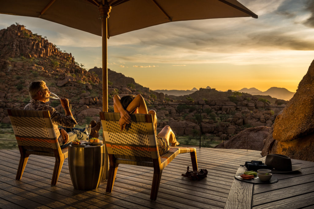 Guests unwind on a Mountain Suite deck at sundown, champagne and snacks close at hand as the boulder-strewn valley glows.